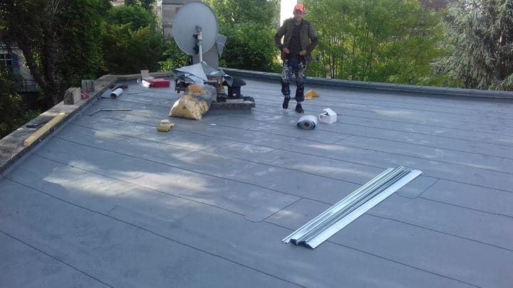 Deux couvreurs déroulant une membrane d'étanchéité sur une toiture-terrasse