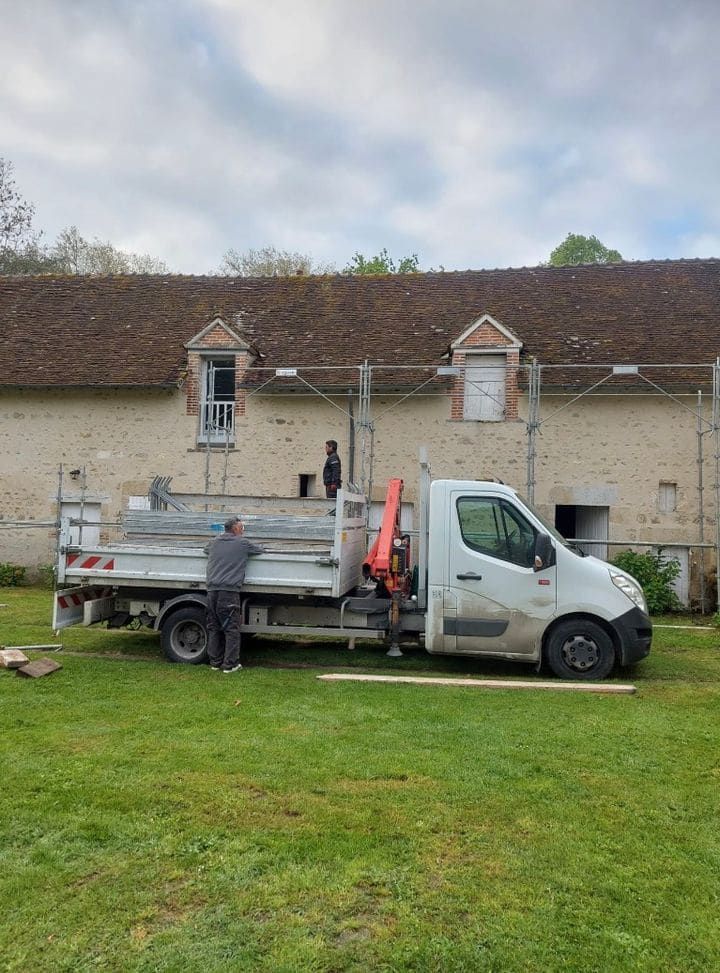Camion benne et fourgon de l'entreprise stationnés devant un chantier
